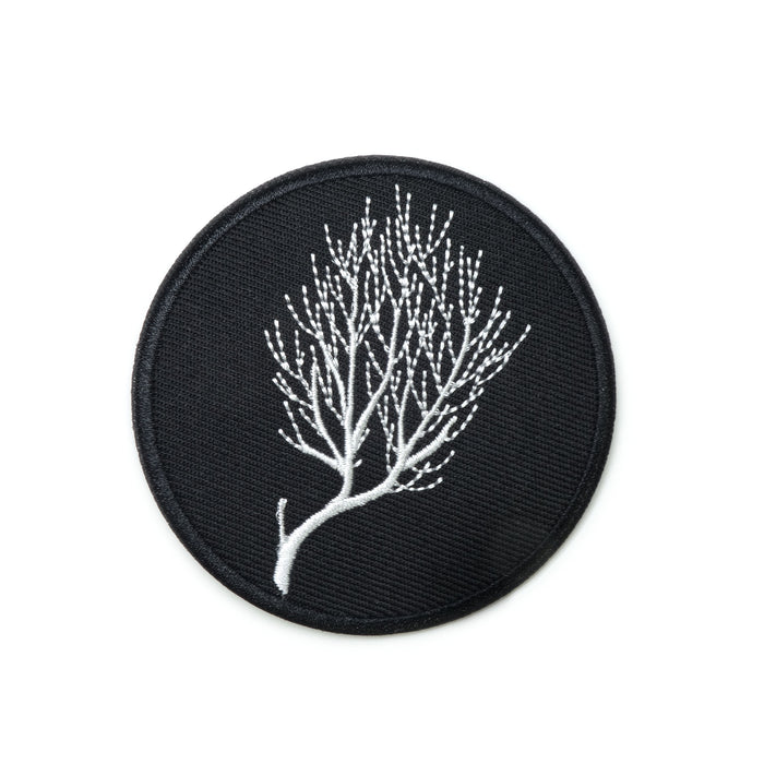 a circular patch, white embroidered lines linework of bare branches of a bush on black background