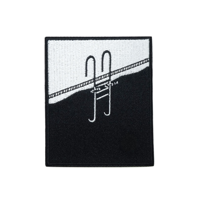 a rectangular embroidered patch in black and white, taller than it is wide, a pool ladder in black emerges out onto the edge of a swimming pool, the submerged portion of the ladder can be seen in white through the black water