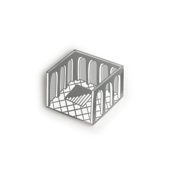 a highly reflective hard enamel pin, a diamond shaped cross-section of a room with no ceiling, arches cut into the walls, tiled floor, and a hole in the floor containing steps leading below, silver outlines, grey negative space for the arches, white tiles and highlights